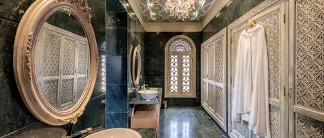 Un baño lujoso con un espejo ovalado grande, un lavabo redondo y un techo decorativo.