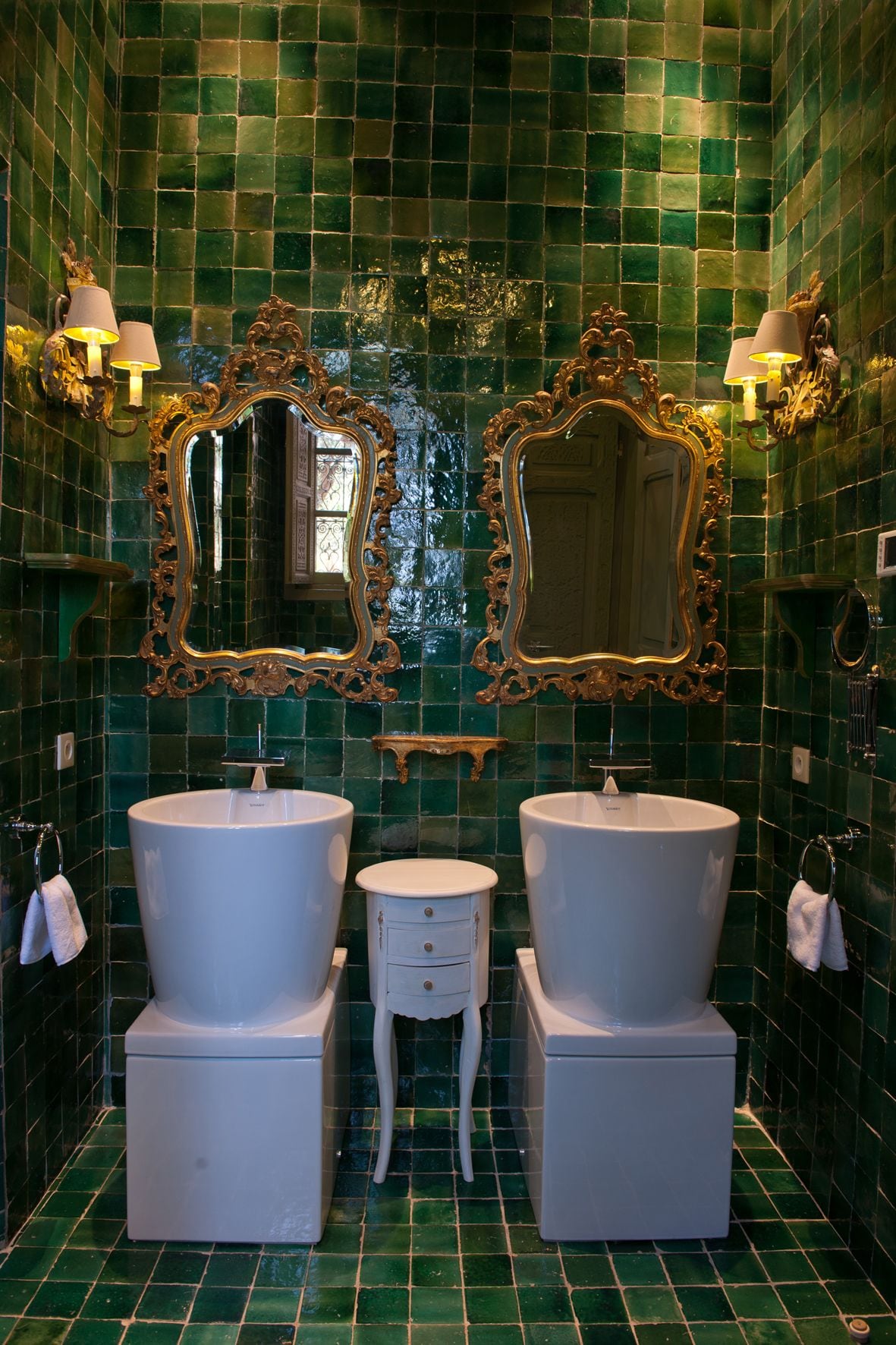 Un baño con dos lavamanos, tocador y espejos decorativos.