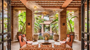 Un amplio salón con zona de estar central, plantas en macetas grandes y vistas a una piscina.