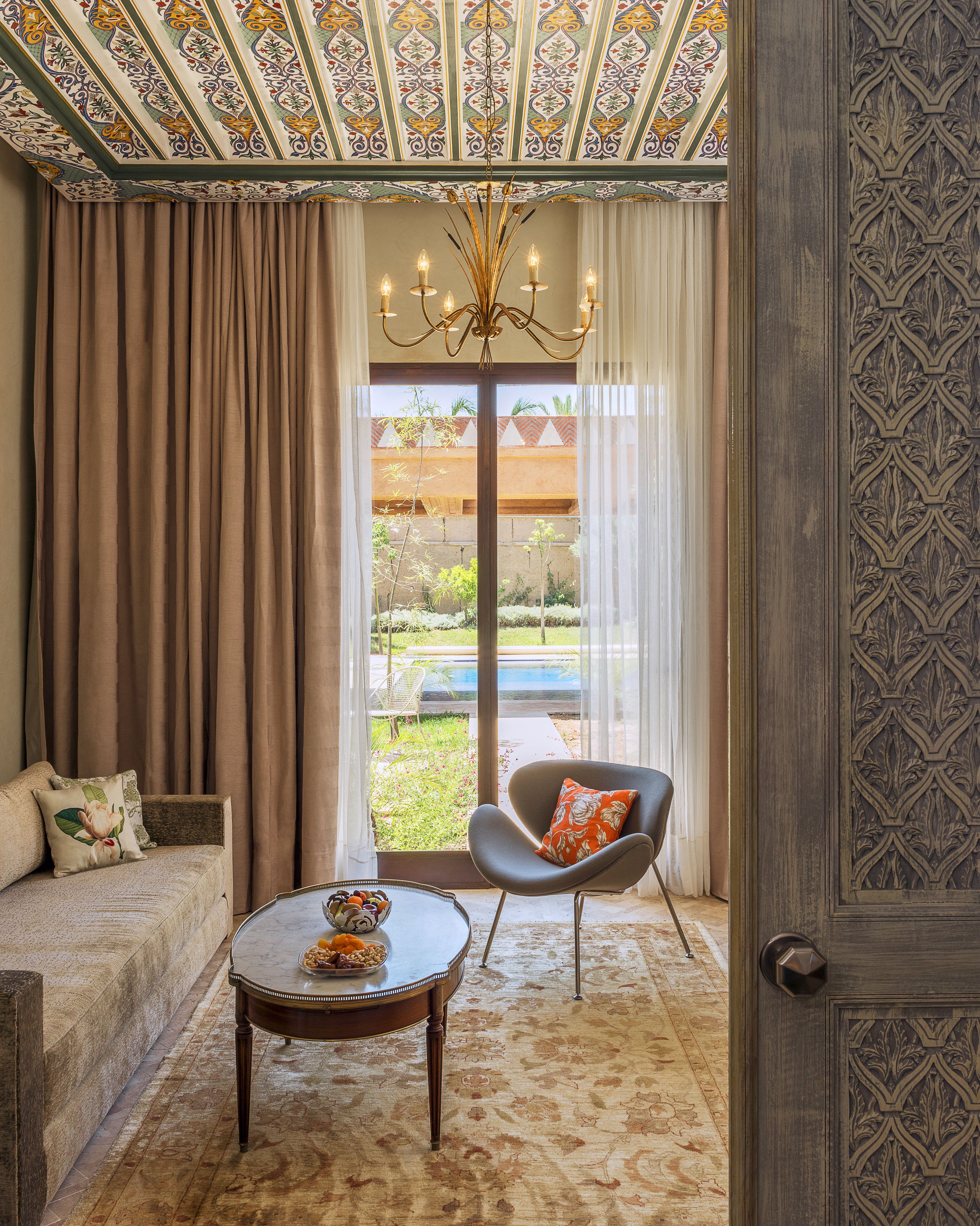 A room with a sofa, a chair, a coffee table, and a view of a garden through a glass door.