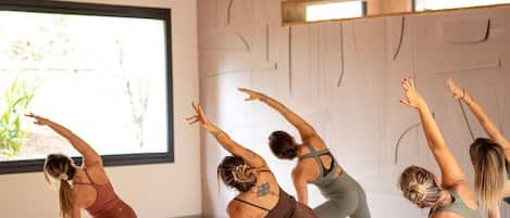 Una clase de yoga en una habitación con vigas de madera y un ventanal grande.