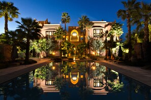A luxurious hotel with a reflective pool, palm trees, and a well-lit entrance. - Tigmiza Boutique Hôtel & Spa (Marrakech)