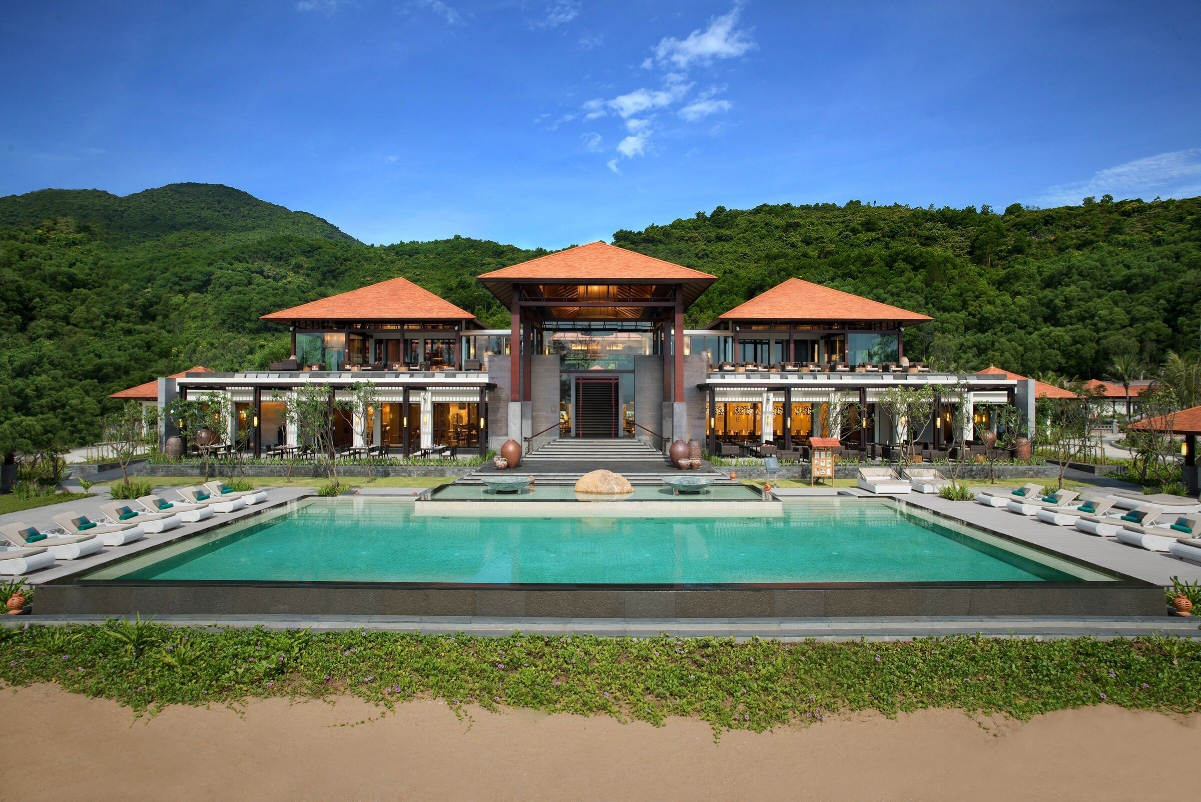 A resort with a large pool, multiple dining areas, and a view of a forested hill.