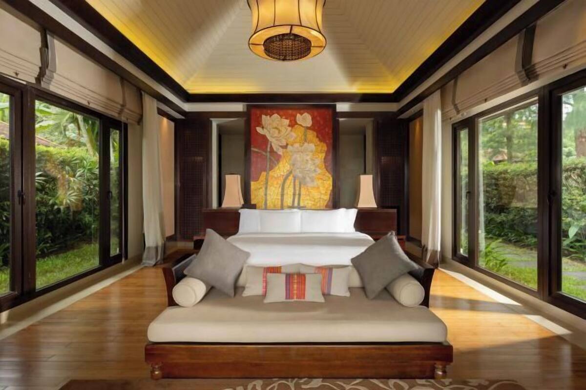 Une chambre spacieuse avec un grand lit, un tableau au-dessus du lit et de grandes fenêtres.
