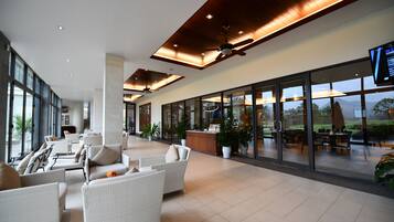A spacious indoor area with wicker furniture, a ceiling fan, and large windows offering a view of the outdoors.