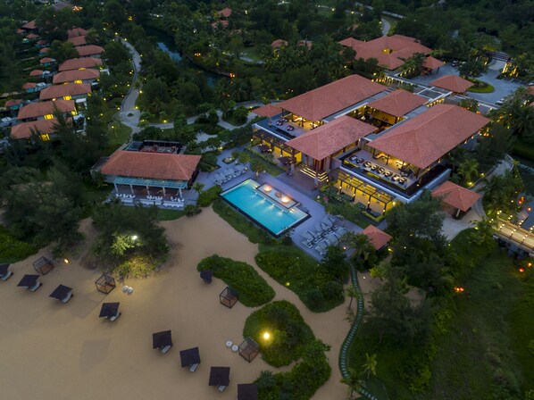 Vista aérea de un resort con varias edificaciones, una piscina y una zona de playa con tumbonas.