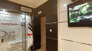 A hotel lobby with a reception desk, a television mounted on the wall, and a sign indicating amenities such as a restaurant and tennis court. - Dar El Ikram (Algiers)