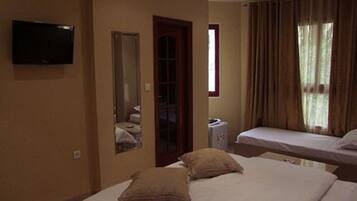 A hotel room with two beds, a TV, a mirror, and a window with curtains.