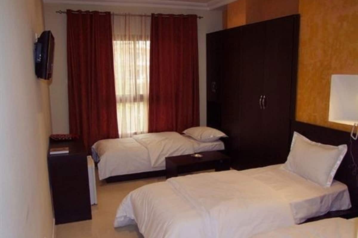 A hotel room with two beds, a wardrobe, a bedside table, and a TV mounted on the wall.