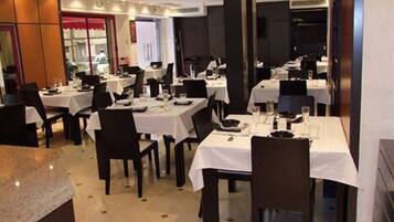 Un restaurant amb diverses taules i cadires, cadascuna coberta amb un mantell blanc i amb plats.