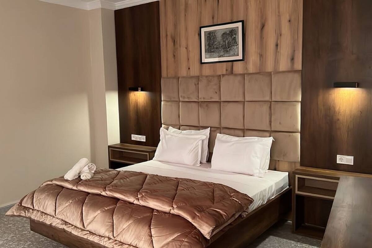 A hotel room with a large bed, a wooden headboard, two bedside lamps, and a framed picture on the wall.