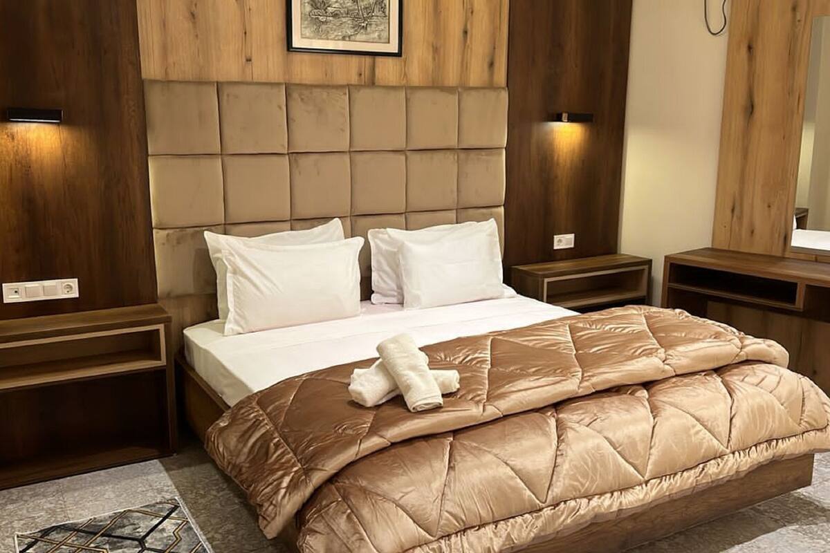 A hotel room with a large bed, wooden headboard, two bedside tables, and a mirror.