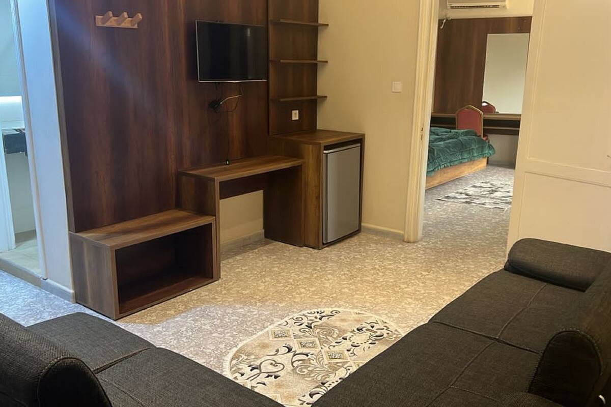 A compact living space with a kitchenette, a TV mounted on the wall, a bed with a green blanket, and a patterned rug.