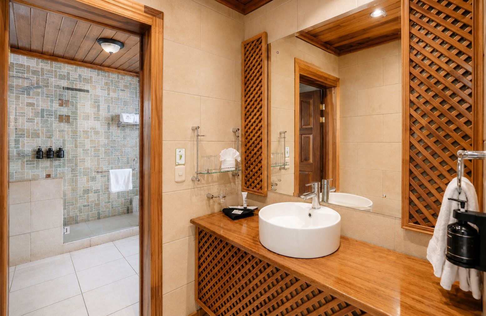 Un baño moderno con ducha de mosaico de piedra, tocador de madera con lavamanos y un espejo grande.