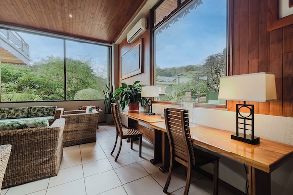 A dining area with wicker furniture, a wooden table, and a view of greenery outside.