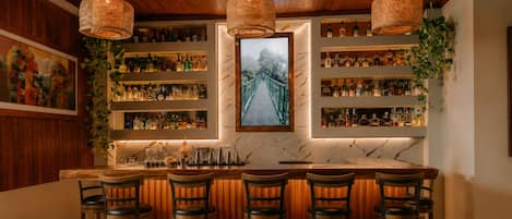 A bar area with wooden bar stools, a marble countertop, and hanging wicker lamps.