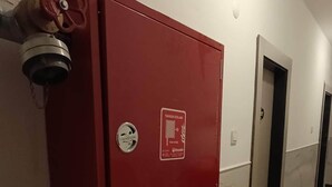 A red fire safety cabinet mounted on a wall in a hallway with marble flooring and doors. - Kleopatra Bebek Hotel (Alanya)