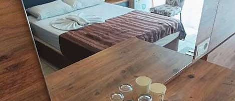 A hotel room with a wooden table, a bed with a blue headboard, a chair, and a window with curtains.