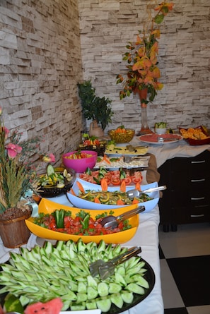 A buffet table with various food items and a potted plant. - Kleopatra Bebek Hotel (Alanya)