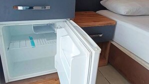 A compact room with a bed, a small wooden nightstand, and a built-in refrigerator. - Kleopatra Bebek Hotel (Alanya)