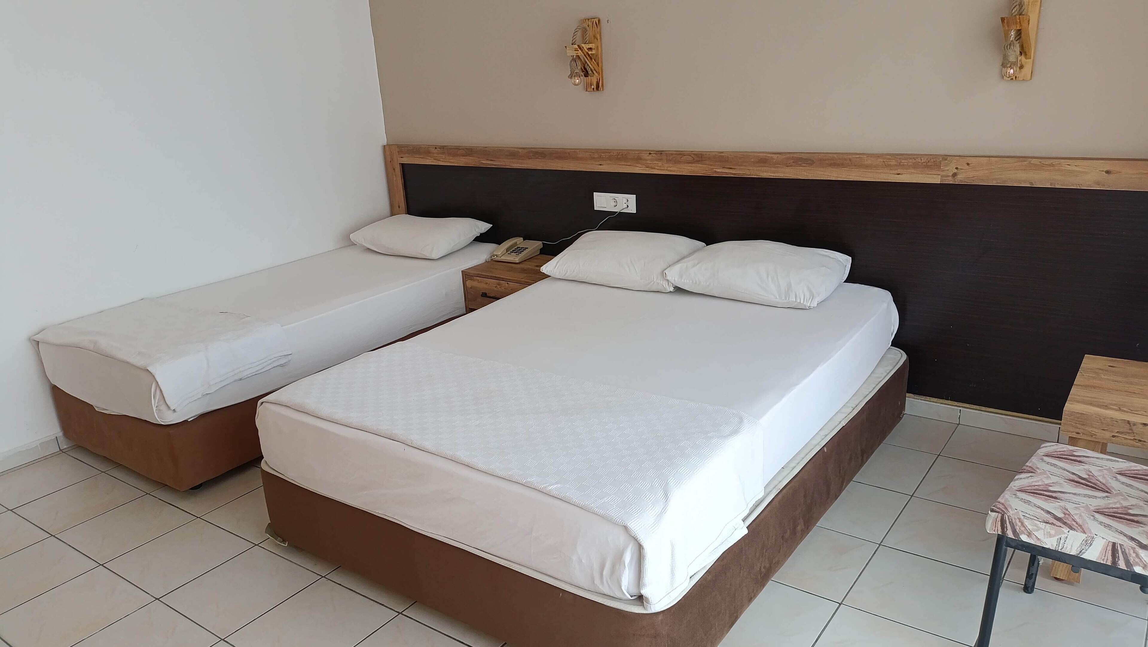 A hotel room with two beds, a wooden headboard, a bedside table with a phone, and a small table with a chair.