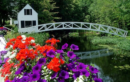 A white house with a white bridge over a pond, surrounded by vibrant flowers.