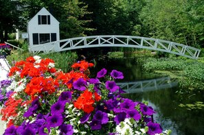 A white house with a white bridge over a pond, surrounded by vibrant flowers. - Kimball Terrace Inn Northeast Harbor (Northeast Harbor)