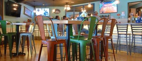 A restaurant interior with multiple tables and chairs, a counter with a menu, and a television screen displaying a sports game.