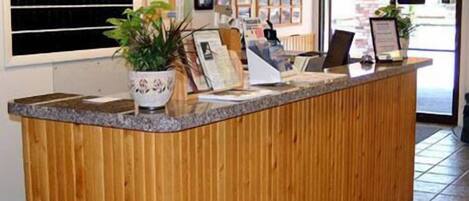 A reception desk with a wooden finish, a potted plant, and framed pictures on the wall.