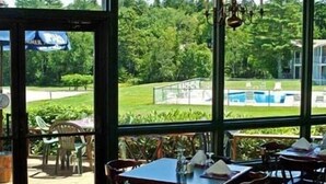An indoor dining area with tables and chairs, large windows offering a view of a swimming pool and greenery. - Kimball Terrace Inn Northeast Harbor (Northeast Harbor)