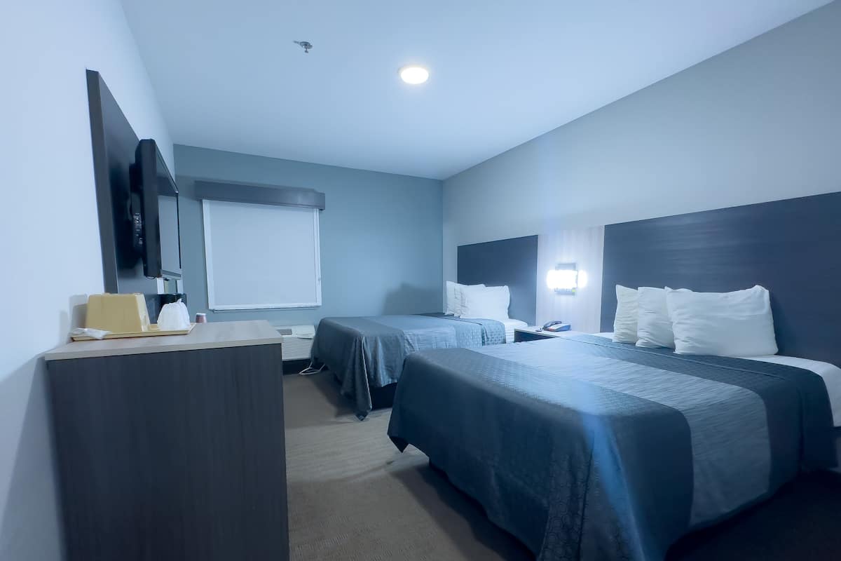 A hotel room with two beds, a desk, a chair, a flat-screen TV, a window, and a ceiling light.