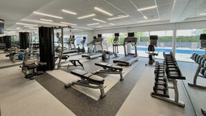 A modern gym with various exercise equipment, large windows, and a view of an outdoor swimming pool. - Courtyard by Marriott San Jose Airport Alajuela (Rio Segundo)