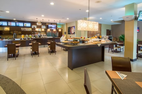 A modern hotel lobby with a central bar area, seating arrangements, and a digital menu display.
