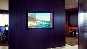 A hotel lobby with a large digital display on the wall, a seating area with a red accent wall, and a carpeted floor. - Courtyard by Marriott San Jose Airport Alajuela (Rio Segundo)