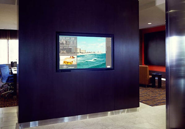 A hotel lobby with a large digital display on the wall, a seating area with a red accent wall, and a carpeted floor. - Courtyard by Marriott San Jose Airport Alajuela (Rio Segundo)