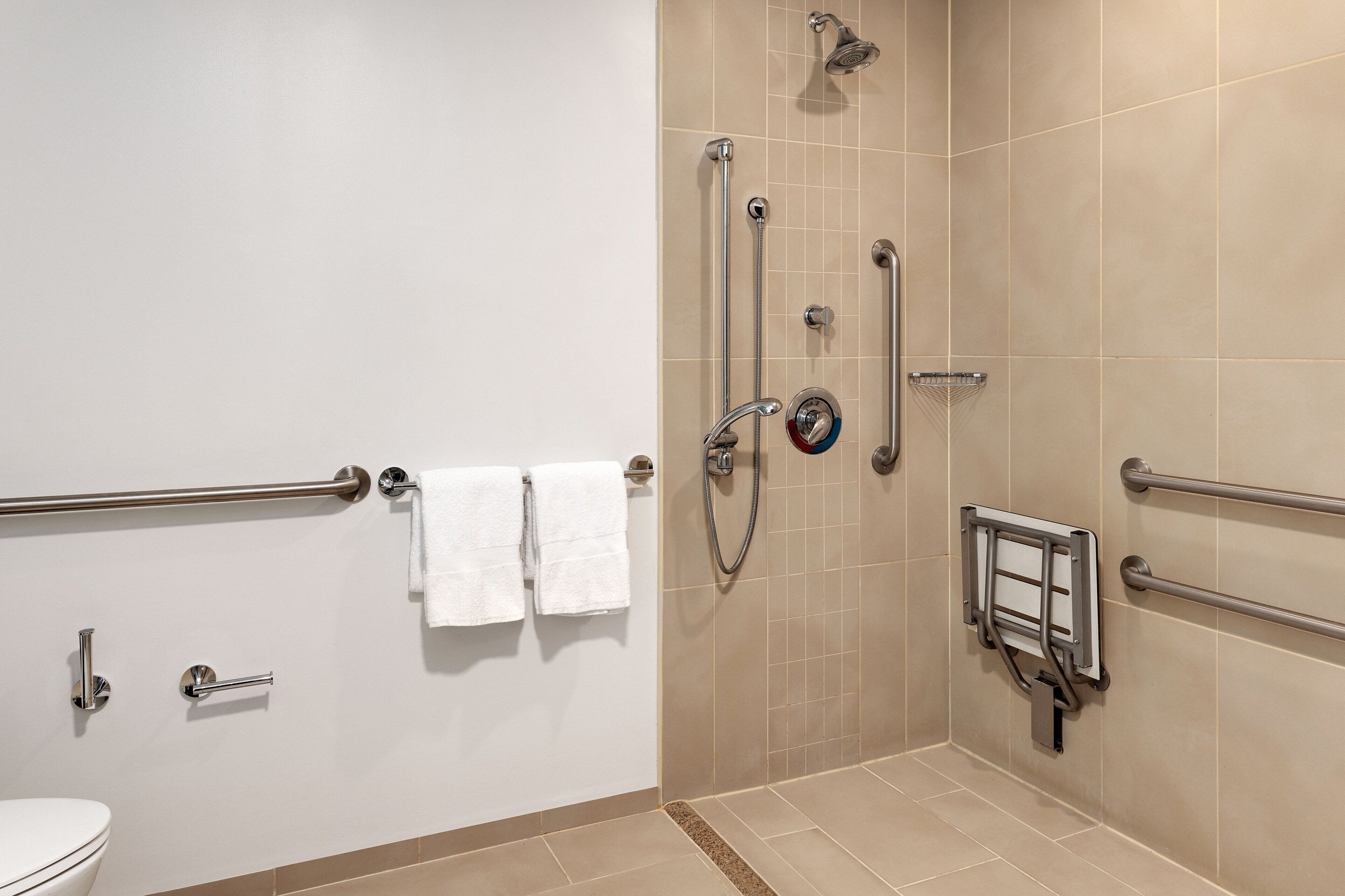 A bathroom with a shower, grab bars, a toilet, and a towel rack.