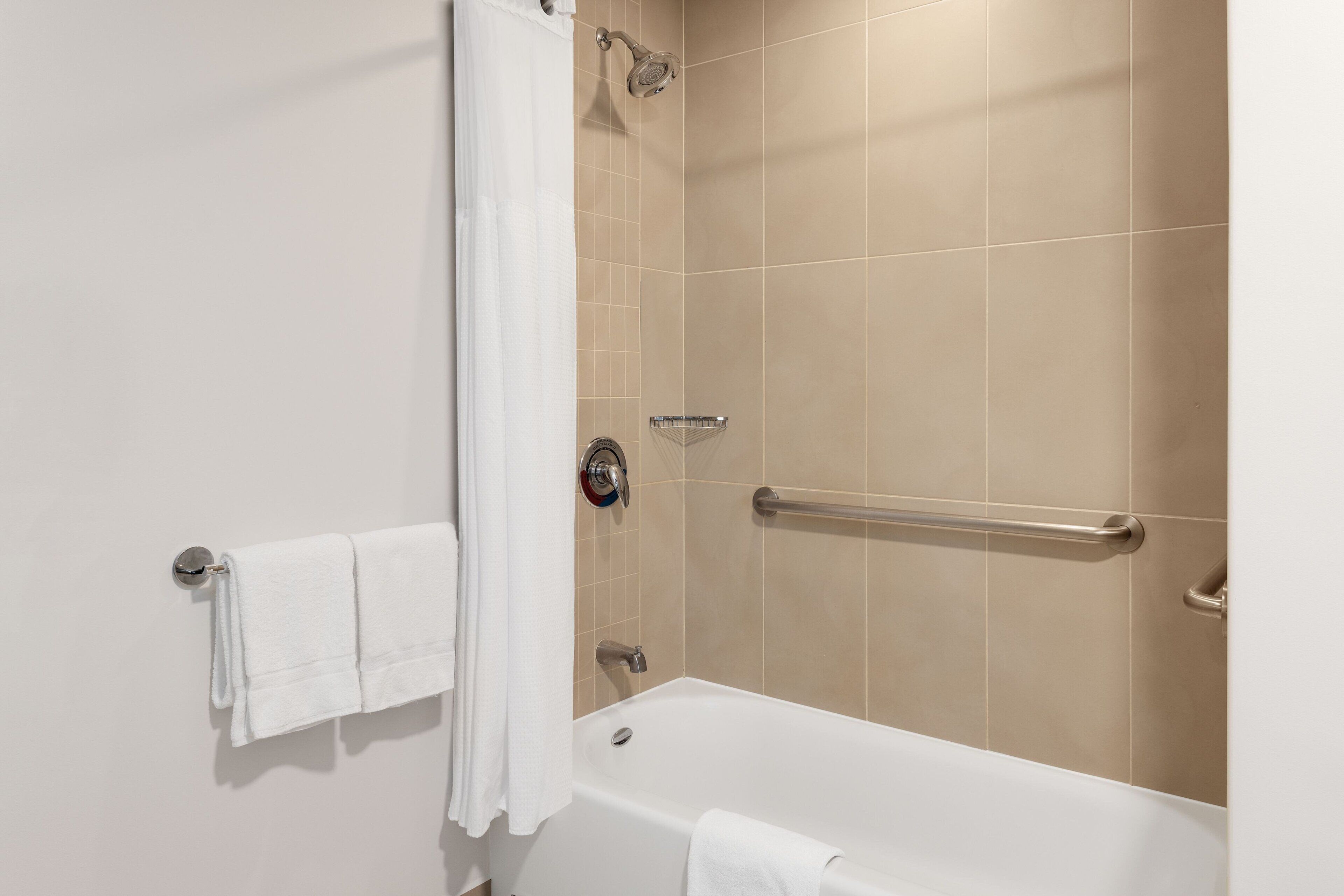 Un bagno moderno con una vasca, una doccia e una barra di sostegno.
