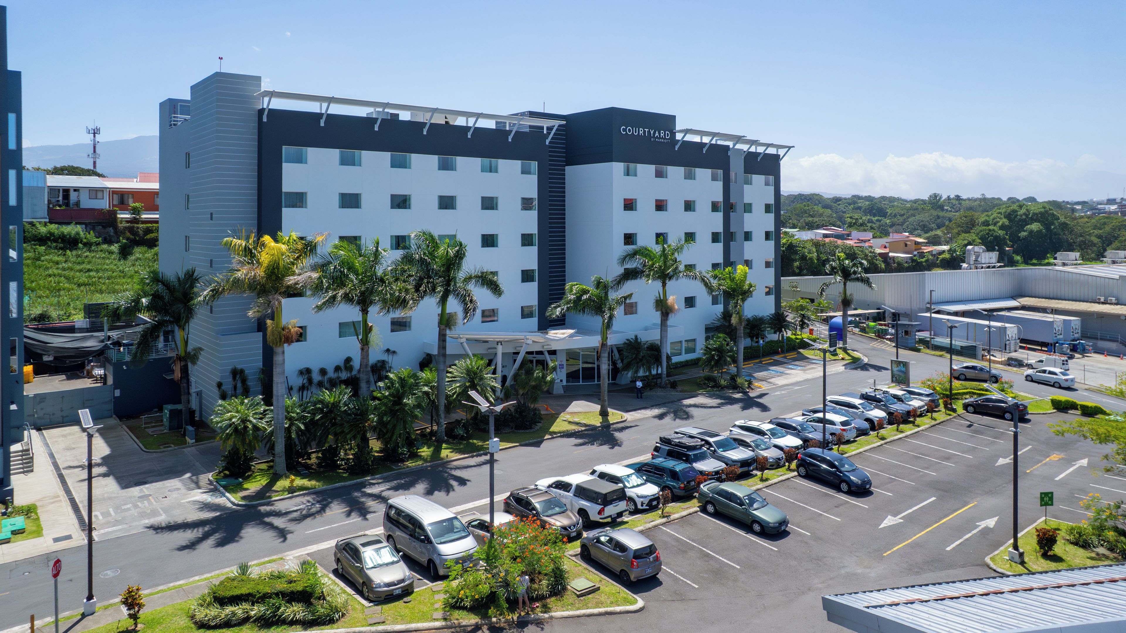 Um hotel com vários andares, estacionamento e palmeiras.