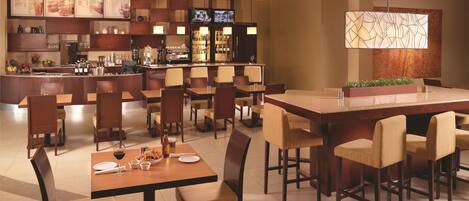 Um restaurante moderno com área de bar, diversas opções de assento e uma tela de televisão.
