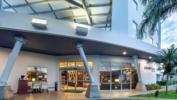 A modern building with a covered entrance, large windows, and a sign reading "COURTYARD." - Courtyard by Marriott San Jose Airport Alajuela (Rio Segundo)