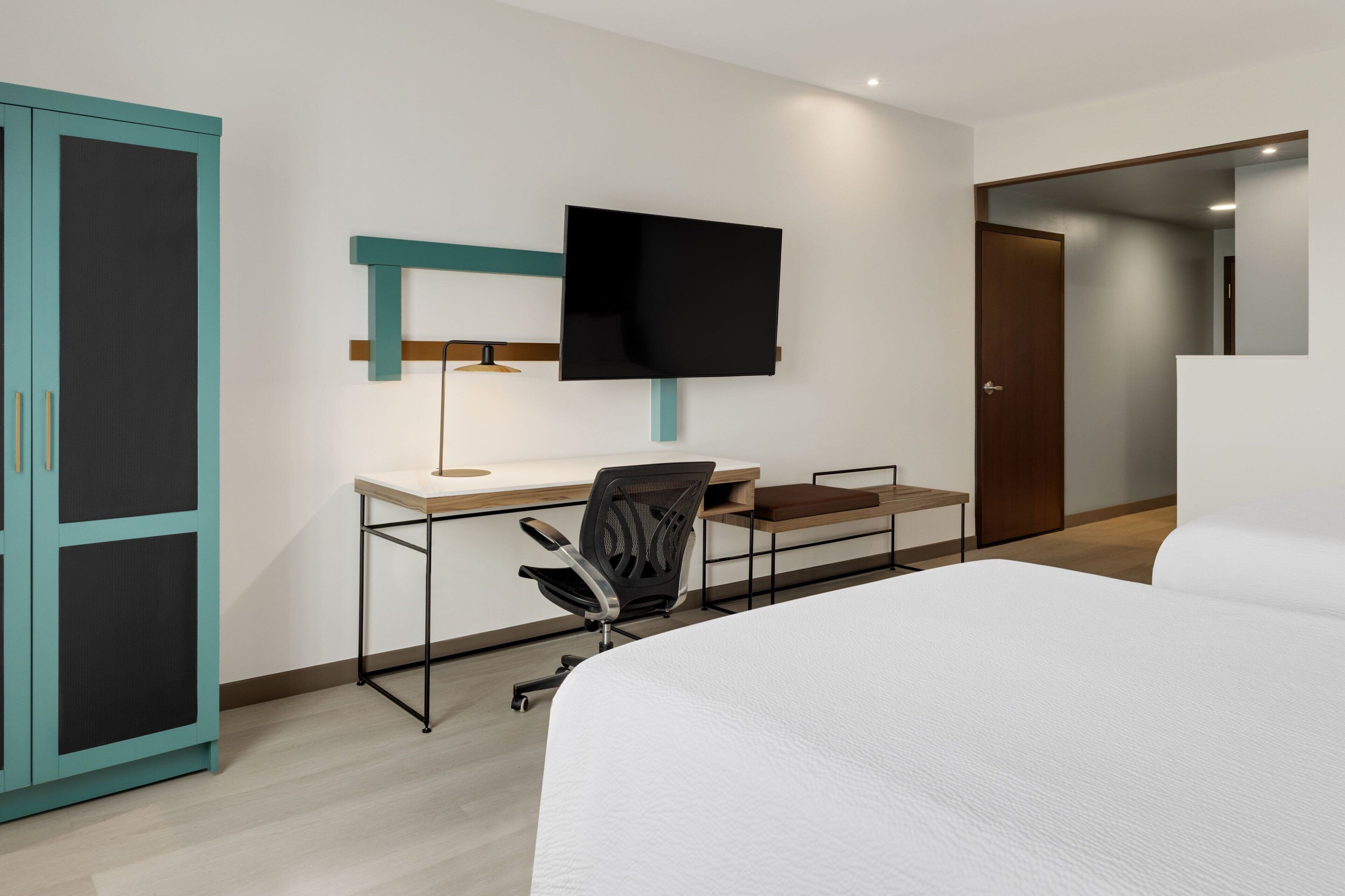 Une chambre d’hôtel comprenant un lit, un bureau avec une chaise, un téléviseur fixé au mur et une armoire.
