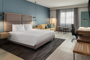 A modern hotel room with a large bed, a sofa, a desk, and a chair.