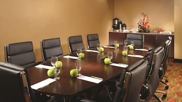 Un salón de conferencias con una larga mesa, sillas de cuero negro y manzanas verdes junto a copas de vino.