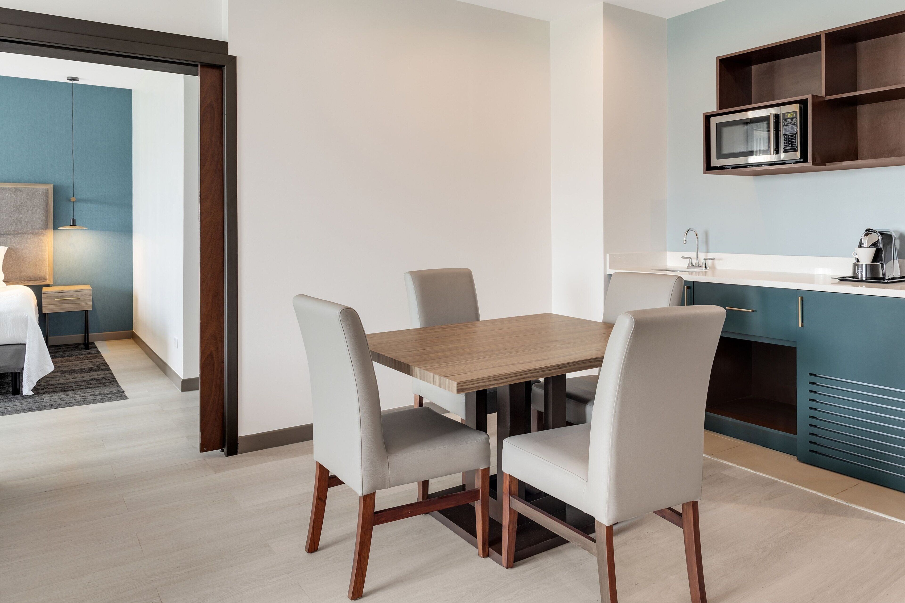 A modern kitchen with a microwave, a sink, and a coffee maker. There is a dining area with a wooden table and four chairs.