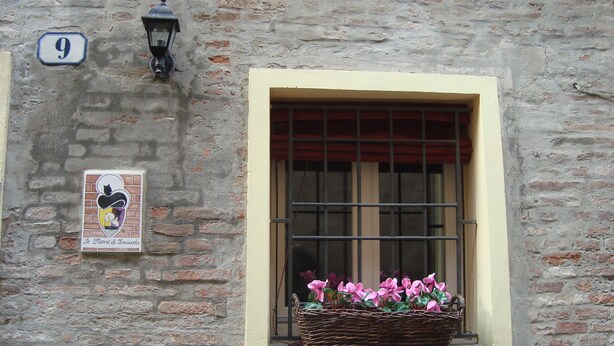 Una ventana con una cesta de mimbre llena de flores rosadas, un cartel con el número 9 y una lámpara fijada a la pared.