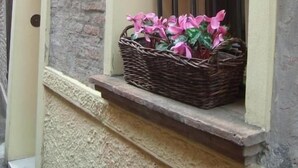Una ventana con una cesta de mimbre que contiene flores rosadas, una lámpara de pared y un cartel.