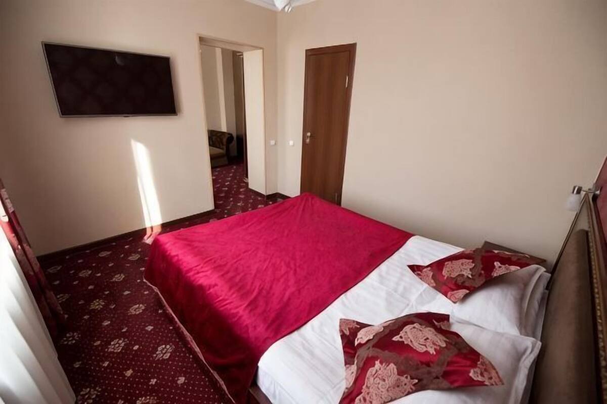 A bedroom with a bed, a television mounted on the wall, and a door leading to another room.
