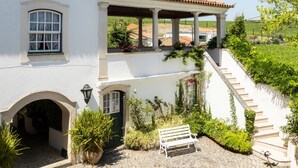 Un edificio bianco con tetto in tegole, una scalinata che conduce a un portico coperto e un cortile in pietra.