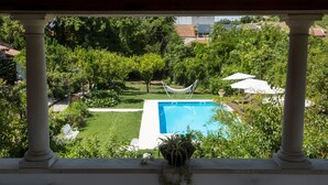 Vista di una piscina circondata da vegetazione lussureggiante, con un’amaca e ombrelloni.