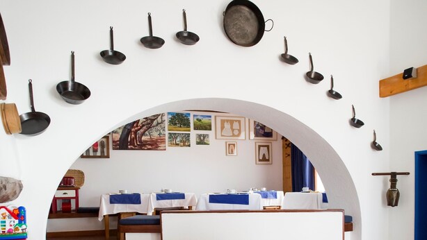Un interior moderno con una zona de estar, una cocina visible a través de un arco, y diversos utensilios de cocina colgados en la pared.